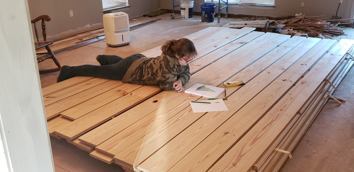 Girl laying on pallet while pine acclimating prior to being glued down and face nailed